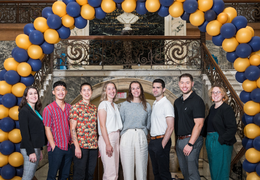 2023 Doctoral Fellows in front of a blue and gold balloon arch in Main Building